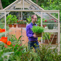 Man moving potted plants infront of Antique ivory greenhouse